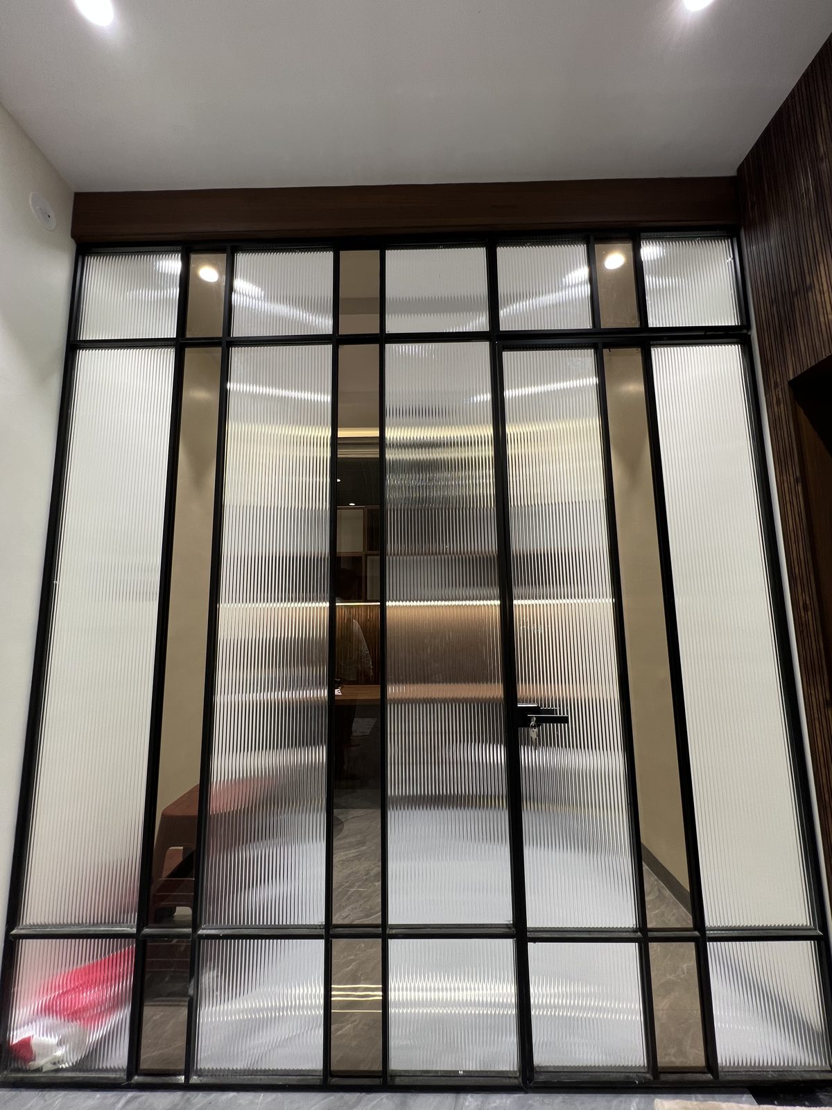 Full height fluted glass partition door with black metal framing and brass detail, Latur