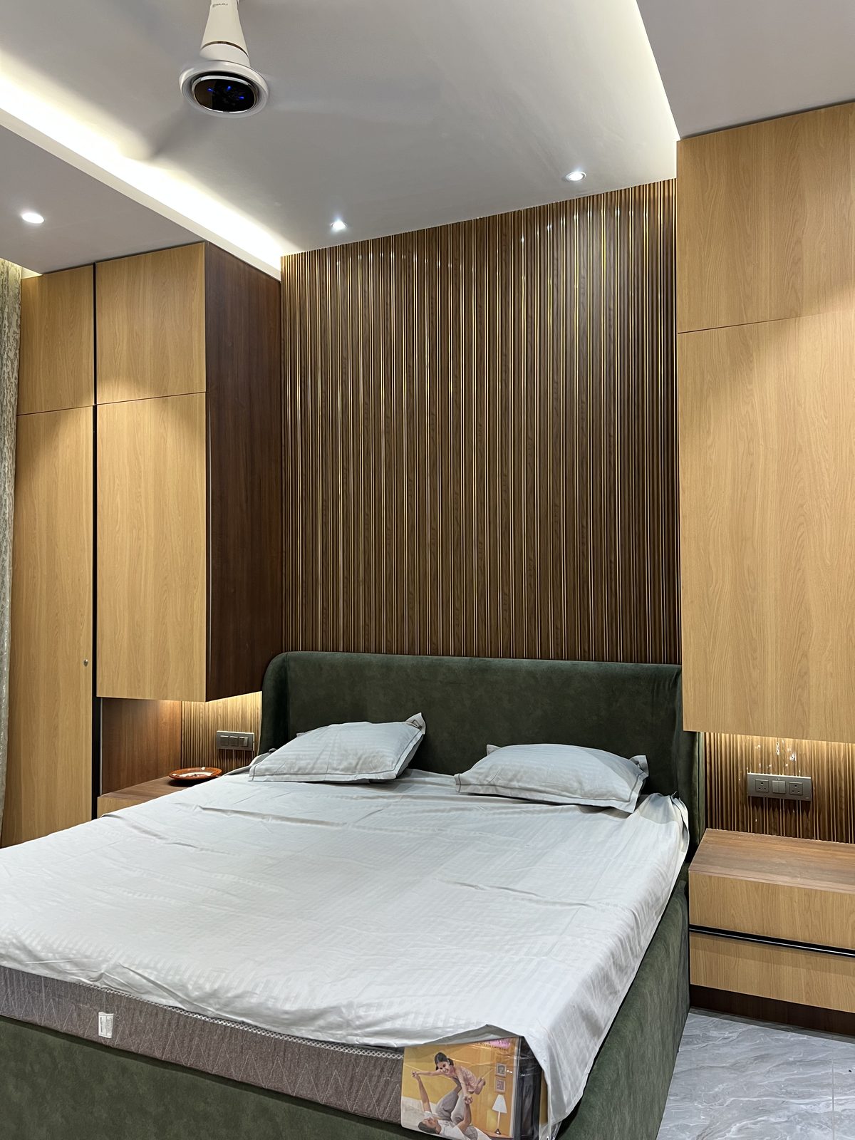 Green velvet upholstered bed against floor to ceiling wooden fluted panelling and wardrobe, Udgir