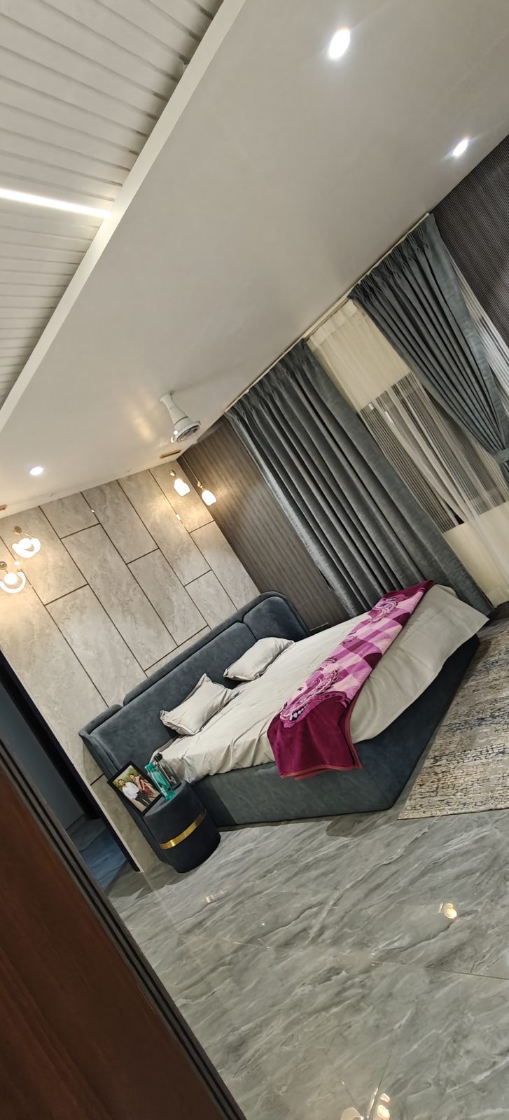 Grey upholstered bed with stone finish wall panel and fitted wardrobe alongside, Udgir