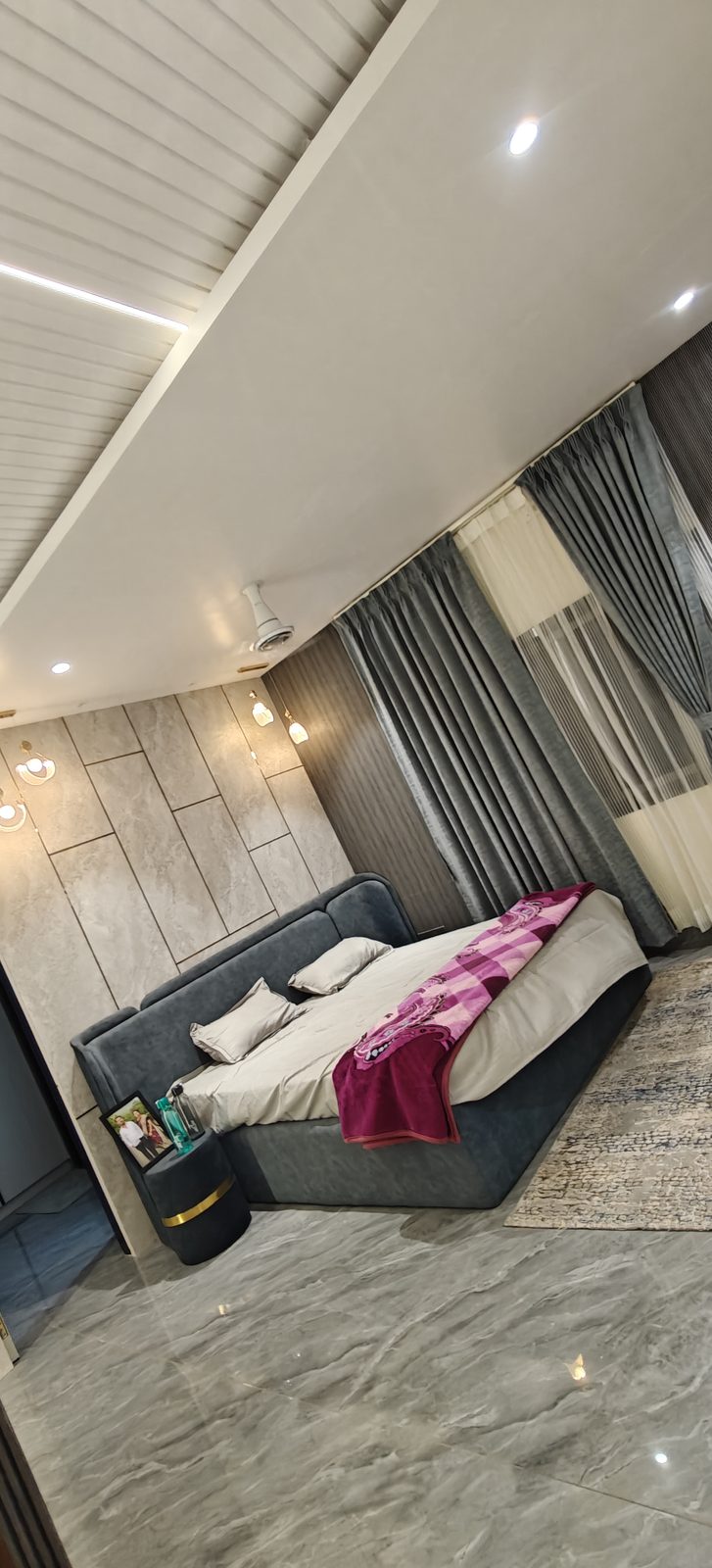 Grey upholstered bed with stone finish feature wall and track lighting in a modern bedroom, Udgir