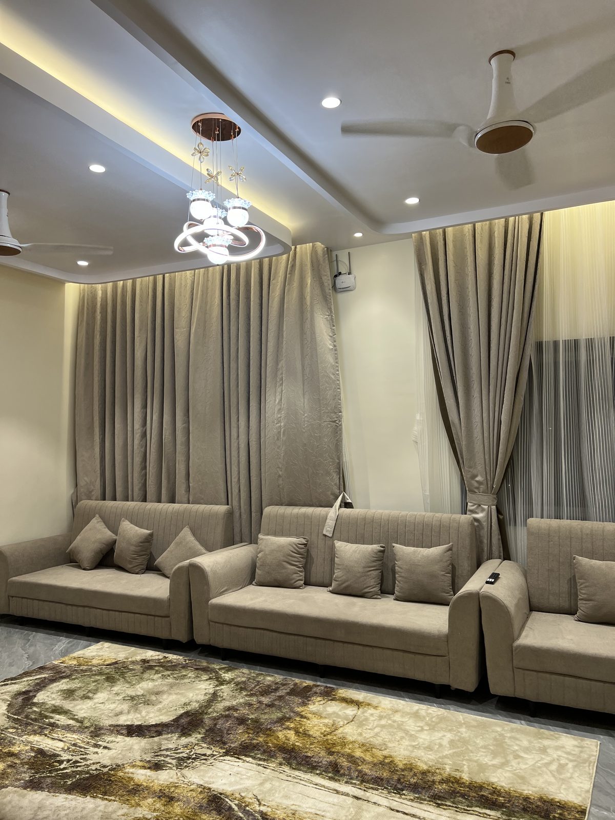 Modular fabric sofa set in a living room with layered curtains and a decorative chandelier, Udgir