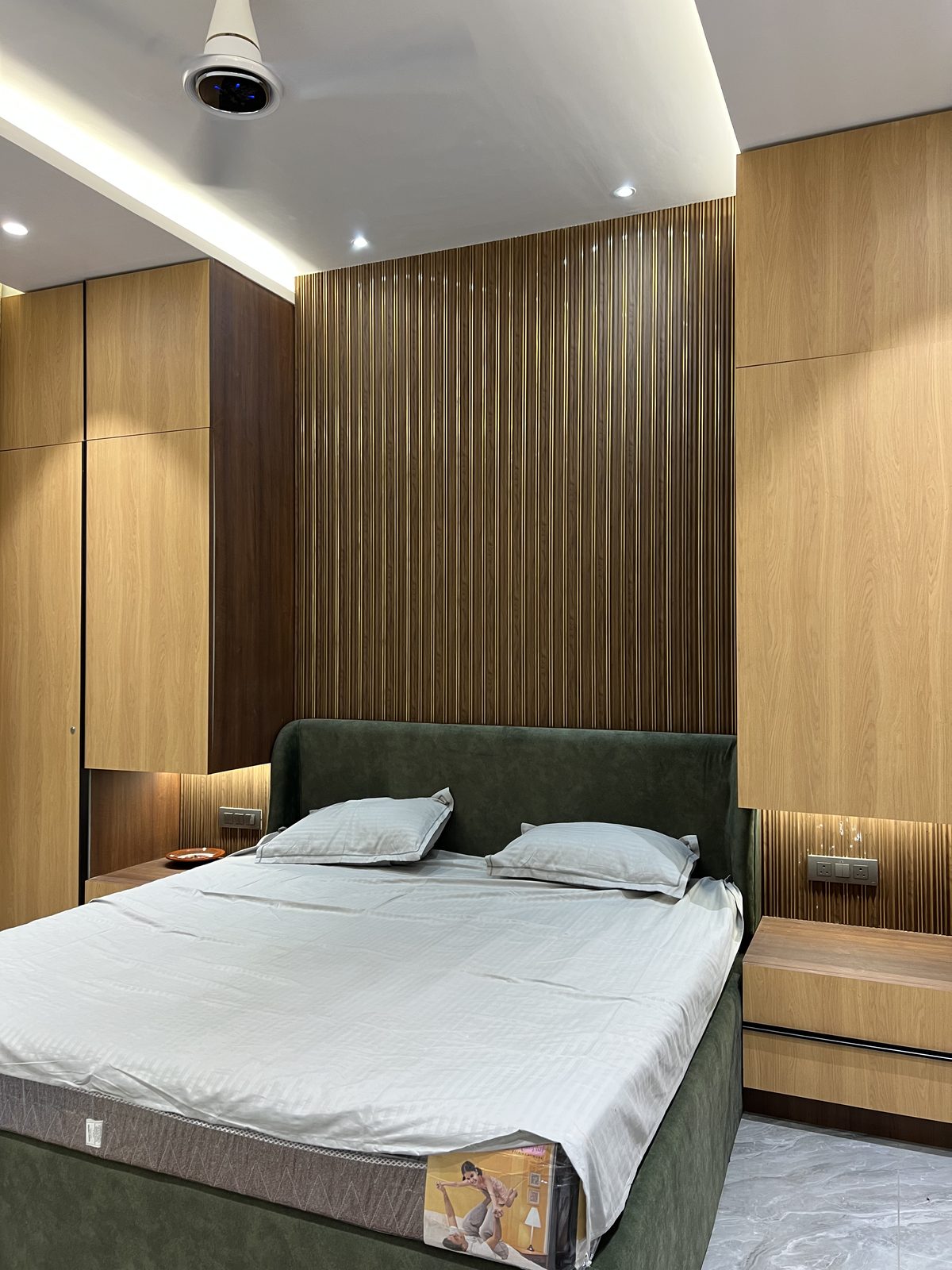 Green velvet bed framed by floor to ceiling wooden wardrobes and fluted panelling, Latur